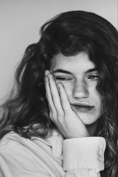 Black and white photo of a woman slightly grimacing as she touches her face.