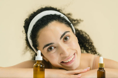 A woman smiles with her head on her hands and two amber dropper bottles in front of her.