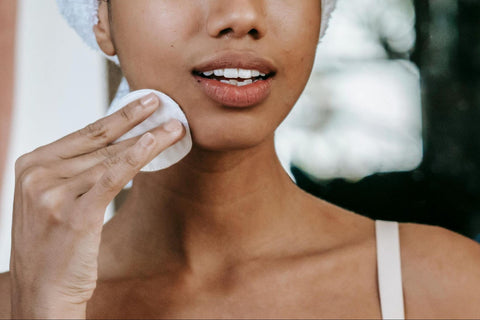 The lower half of a woman’s face as she uses a cotton circle to wipe her face.