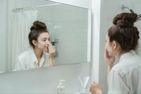 A woman with a messy bun scrubs her face with soap-covered hands.