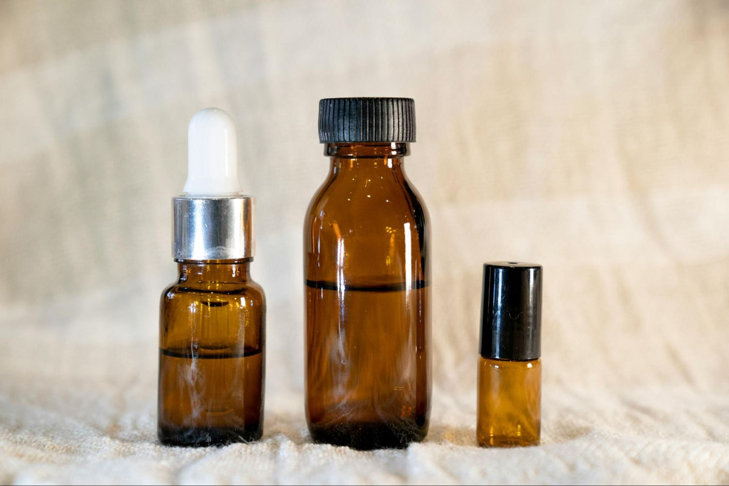 Three amber bottles of different sizes sit in a row with various amounts of serum inside.