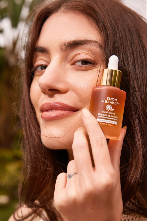 A woman holds up a niacinamide-containing serum beside her clean and healthy skin.