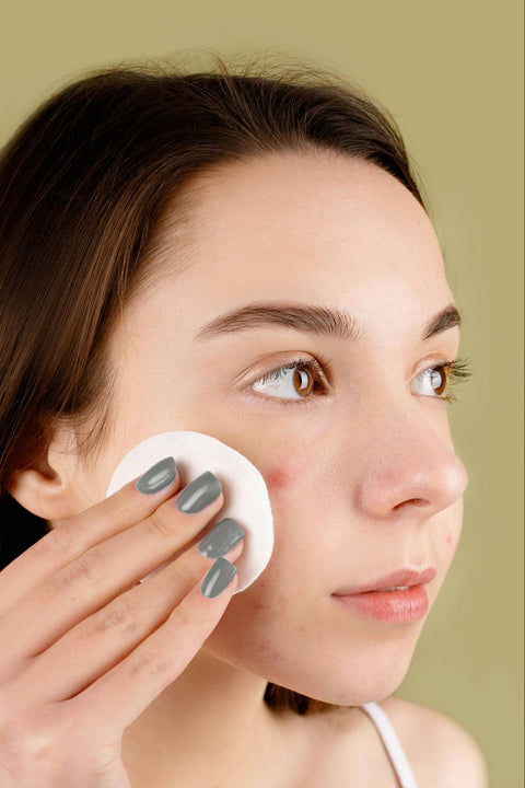 A woman uses a cotton facial circle on her cheek.